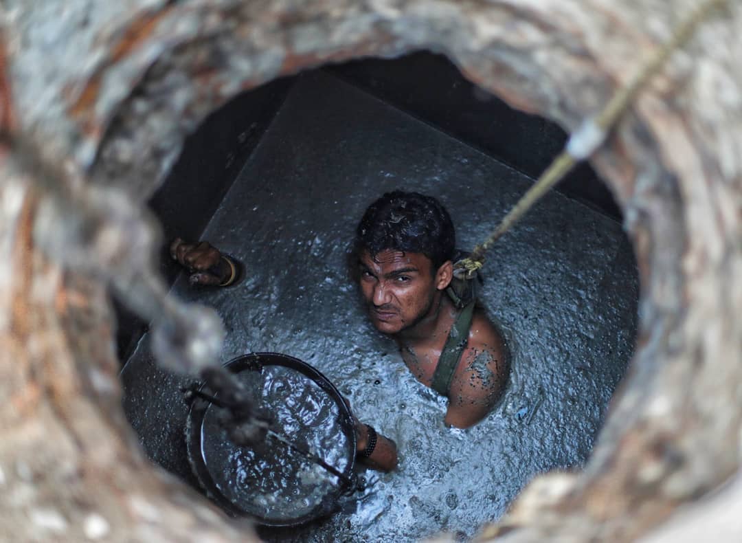 A manual scavenger inside a septic tank with no protective equipment.